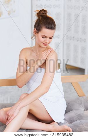 Cute Caucasian Woman In White Towel Applying Cream On Her Skin Before Spa Procedure On The White Sal