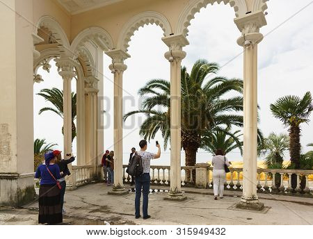 Gagra, Abkhazia - May 02, 2019: People Are Photographed Against The Background Of The Old Colonnade 