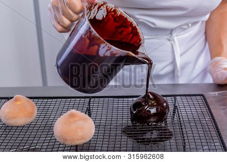 The Pastry Chef In The Kitchen Glazes Pastries. Cook Pours Chocolate Icing From A Bowl Onto Cakes. M