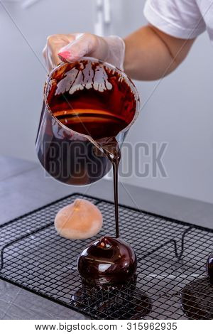 The Pastry Chef In The Kitchen Glazes Pastries. Cook Pours Chocolate Icing From A Bowl Onto Cakes. M