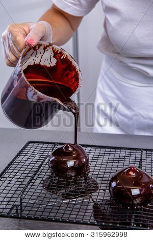 The Pastry Chef In The Kitchen Glazes Pastries. Cook Pours Chocolate Icing From A Bowl Onto Cakes. M