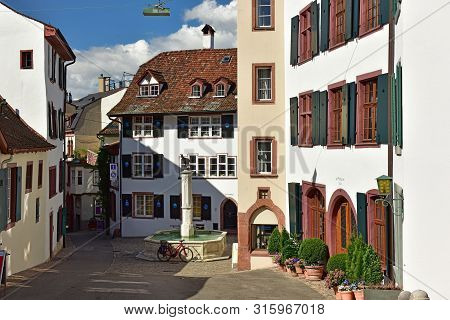 BASEL, SWITZERLAND - APRIL 17, 2019. Old town. Gems-Brunnen fountain on the Gemsberg street surrounded by the beautiful medieval houses. Grossbasel district, city of Basel, Switzerland, Europe