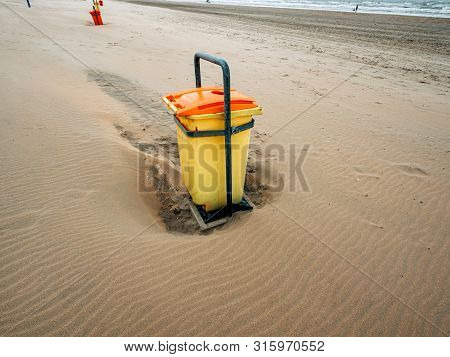Side View Of Modern Yellow Garbage Bin Waste Collection On The Sand Beach In Netherlands In The Over