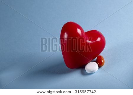 The Figure Of A Red Heart And Two Pills On A Blue Background. Horizontal, Close-up, Free Space, No P