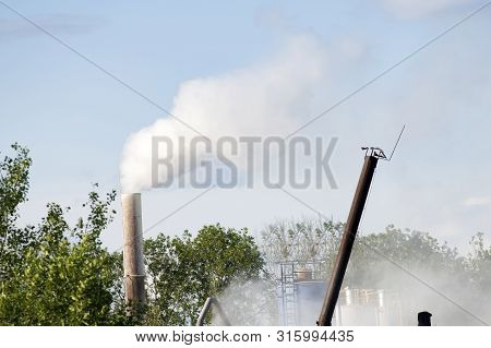 Smoke, Air Emissions From An Industrial Pipe Against Green Trees. Pollution Of The Environmen.