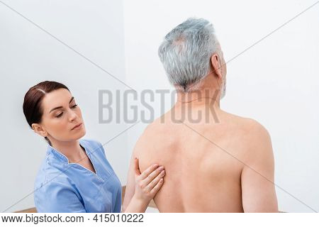Rehabilitologist Examining Back Of Mature Man In Hospital.