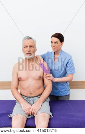 Rehabilitologist Making Kinesiotaping Procedure On Middle Aged Man.