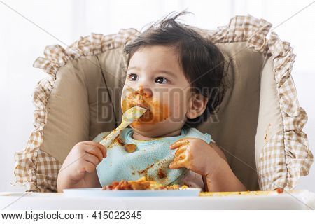 Adorable Little Child Funny Girl Eating Spaghetti With Spoon While Sitting In High-powered Chair At 