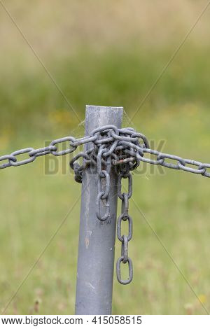 Industrial Chain Attached To A Galvanised Fence Post In A Green Field