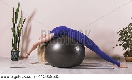 Attractive Woman In Blue Sportswear Practices Yoga, Performing Bridge Pose, Bandhasana On Fitball In