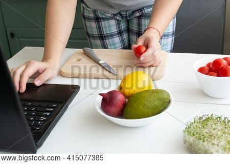 A Woman Is Looking For A Recipe For Vegetarian Alat On A Laptop. The Ingredients Are On The Table. O