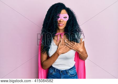Middle age african american woman wearing super hero costume smiling with hands on chest with closed eyes and grateful gesture on face. health concept. 