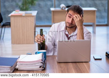 Young male alcohol addicted employee working in the office