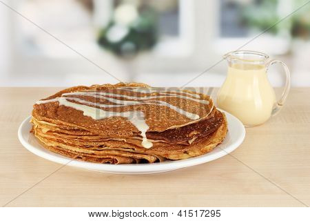 หวาน pancakes บนแผ่นกับนมข้นบนโต๊ะในห้องครัว
