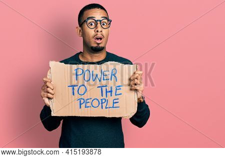 Young african american man holding power to the people banner afraid and shocked with surprise and amazed expression, fear and excited face. 
