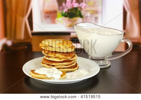 หวาน pancakes บนแผ่น ด้วยครีมเปรี้ยวบนโต๊ะในห้อง