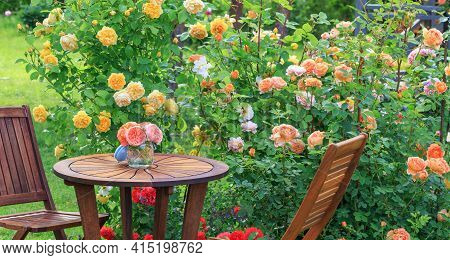 Romantic Sitting Area In The Rose Garden, Round Wooden Table And Chairs Near The Large Flowering Bus