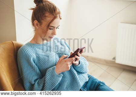 Ginger Ccaucasian Woman With Freckles Is Chatting On Mobile While Lying On A Armchair At Home