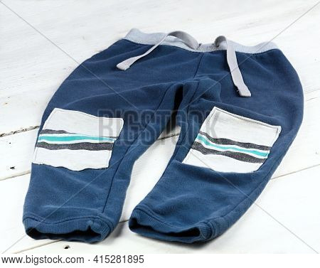 Children Sweatpants Mended With Patches.  Patch With Stripes On Blue Worn Sweatsuit.