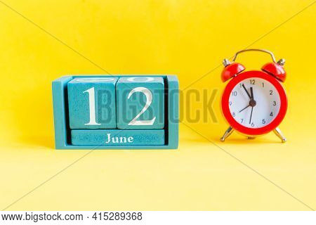 June 12. Blue Cube Calendar With Month Date And Alarm Clock On Bright Yellow Background