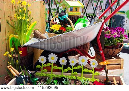 Various Garden Tools And Decor. Household Goods In A Wheelbarrow Trolley Flowers, Watering, Goloshes