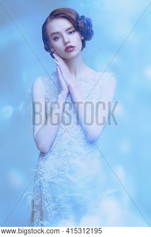 Portrait of a charming young woman in a luxury white dress on a light blue background. Hair and makeup in the style of the 20s. Evening makeup and hairstyle. 