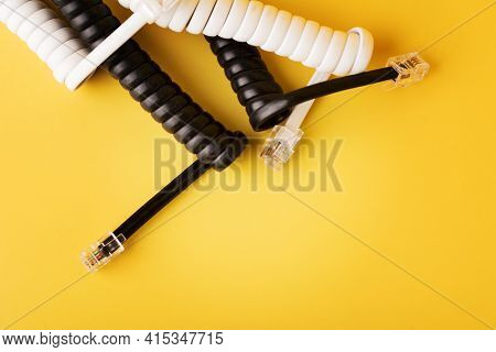 Compressed Black And White Spiral Phone Cord With Connectors On Yellow Background. Twisted Telephone