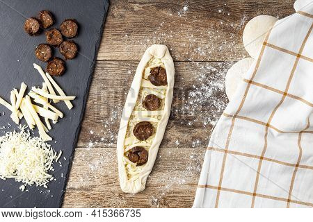 A Woman Is Placing Ingredients On Flattened Dough On Wood Kitchen Countertop. A Bread Making Concept