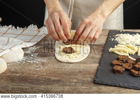 A Woman Is Placing Ingredients On Flattened Dough On Wood Kitchen Countertop. A Bread Making Concept