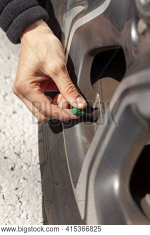 A Caucasian Woman Is Removing Or Attaching The Green Tire Stem Valve Cap Of Her Vehicle. This Is Don
