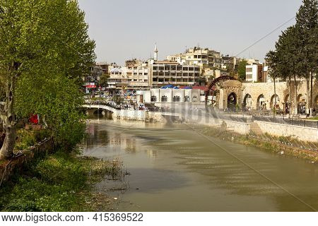 Hama, Syria 04-02-2010: Cityscape Featuring The Orontes River And Arched Stone Bridge Over It. There