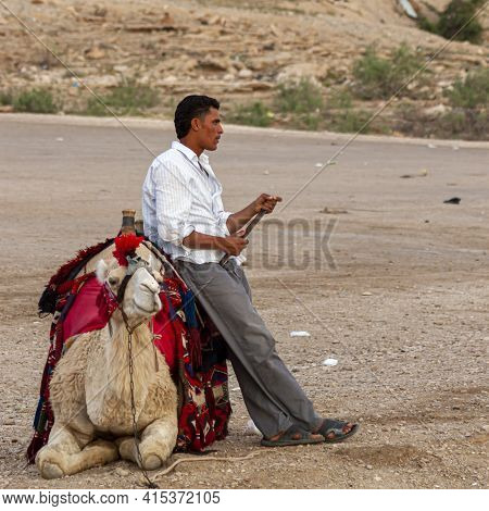 Petra, Jordan 04/01/2010: A Bedouin Tourist Guide Is Leaning Onto His Camel Waiting For Tourist Cust