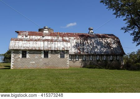 An Abandoned Old Farm House With A Tall Brick Silo And A Big Barn With Rusted Tin Ceiling. This Very