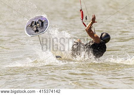 A Kitesurfer Wearing Protective Equipment Is Losing Balance And Falling Off The Board Into The Sea O