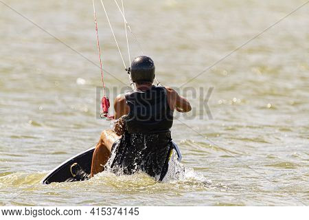 A Kitesurfer Wearing Protective Equipment Is Losing Balance And Falling Off The Board Into The Sea O