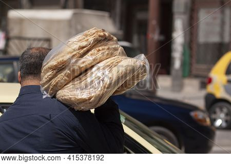 A Syrian Baker Is Carrying  Fresh Made Traditional Flat Breads In The Street. The Breads Are Stacked