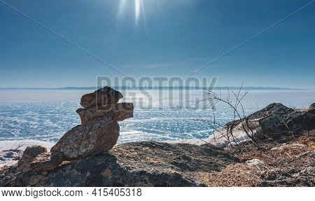 The Blue Ice Of The Lake Is Covered With Snow Like Lace. In The Foreground Is A Pyramid Made Of Ston