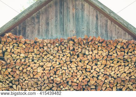 Firewood Or Fuelwood Stacked By A Wall. Wooden Pile Prepared For Winter. Fuel For Countryside Firepl