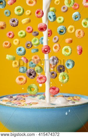 Dropping Cereals And Pouring Milk Into A Blue Bowl, Isolated On An Orange Background. Preparing Brea