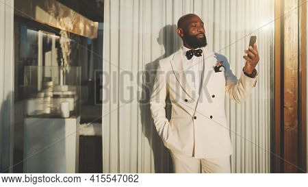 An Outdoor Portrait Of A Dapper Cheerful Mature Bald Bearded Black Guy In An Elegant White Suit, Hav