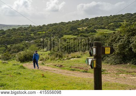 A Hiker On A Nature Path In The Adullam Region Of Israel, Passing Near A Direction Sign, On A Hazy D