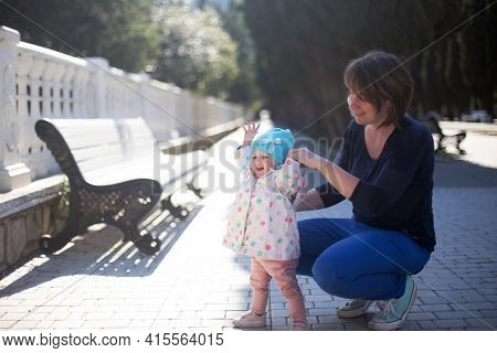 Mother And Her Small One Year Old Daughter Learning How To Walk. Baby First Steps, Mom Is Holding He