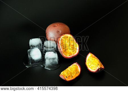 Ripe Passion Fruit Whole And Cut Into Slices And Cubes Of Melted Ice On A Black Isolated Background.