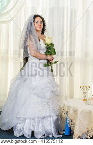 A Jewish Bride Stands In A Synagogue At A Table With Flowers Before A Chuppa Ceremony During A Pande