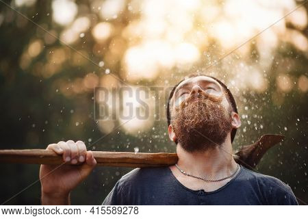 A Bearded Man In A Dark Sleeveless T-shirt With A Large Mustache And Gray Hair Holds An Iron Ax On H