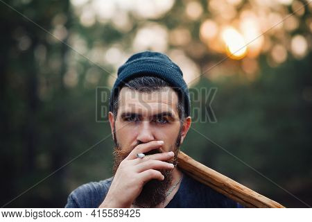 Adult Bearded Stylish Man In A Dark Sleeveless T-shirt And In A Warm Hat With A Large Mustache And G