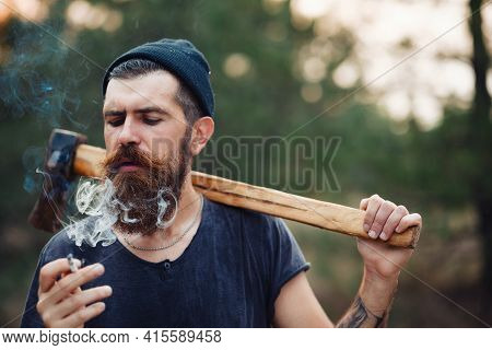 A Stylish Bearded Man In A Dark Sleeveless T-shirt And In A Warm Hat With A Large Mustache And Gray