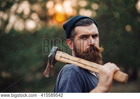 A Serious Man With A Thick Beard And A Large Mustache In A Dark Sleeveless T-shirt And A Warm Hat Wi