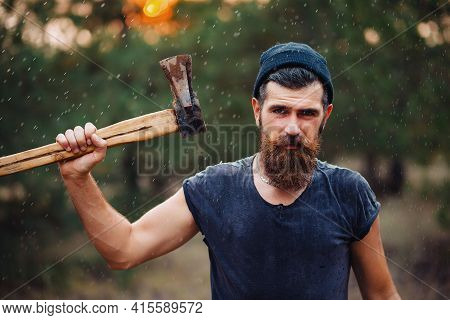 A Serious Man With A Thick Beard And A Large Mustache In A Dark Sleeveless T-shirt And A Warm Hat Wi