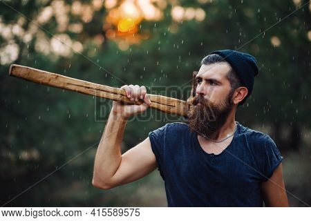 Man With A Thick Beard And A Large Mustache In A Dark Sleeveless T-shirt And A Warm Hat With Gray Ha